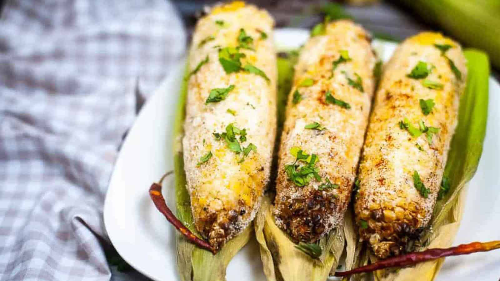 Low angle shot of 3 ears of corn elote on corn husks.