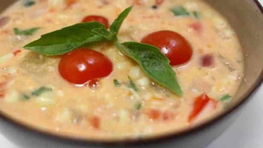 A bowl of corn and tomato soup with fresh basil.