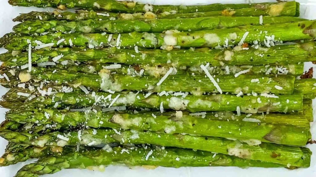 Asparagus spears with parmesan and garlic on a white plate.