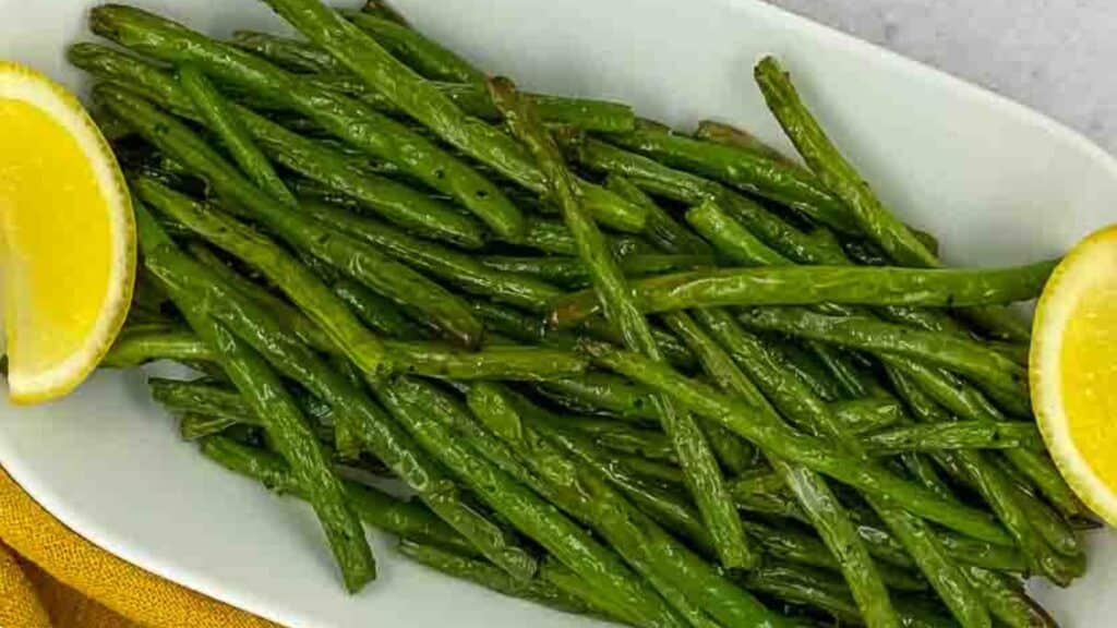 Grilled green beans on a white plate with lemon wedges.