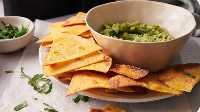 Air fried tortilla chips stacked on a plate around a bowl of dipping sauce.