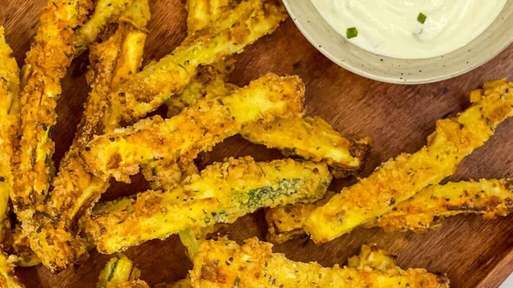 Zucchini fries with dipping sauce on a wooden board.