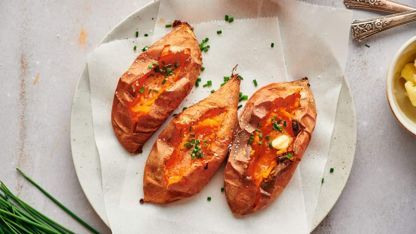 Three baked sweet potatoes with butter and chives on.