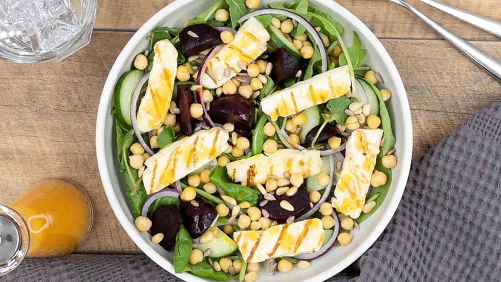 Sliced halloumi cheese, beets and greens in a white ceramic bowl.