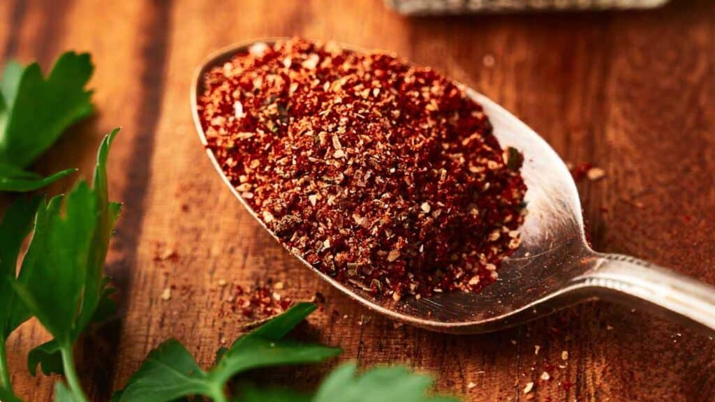 A spoon with red pepper and parsley on a wooden table.