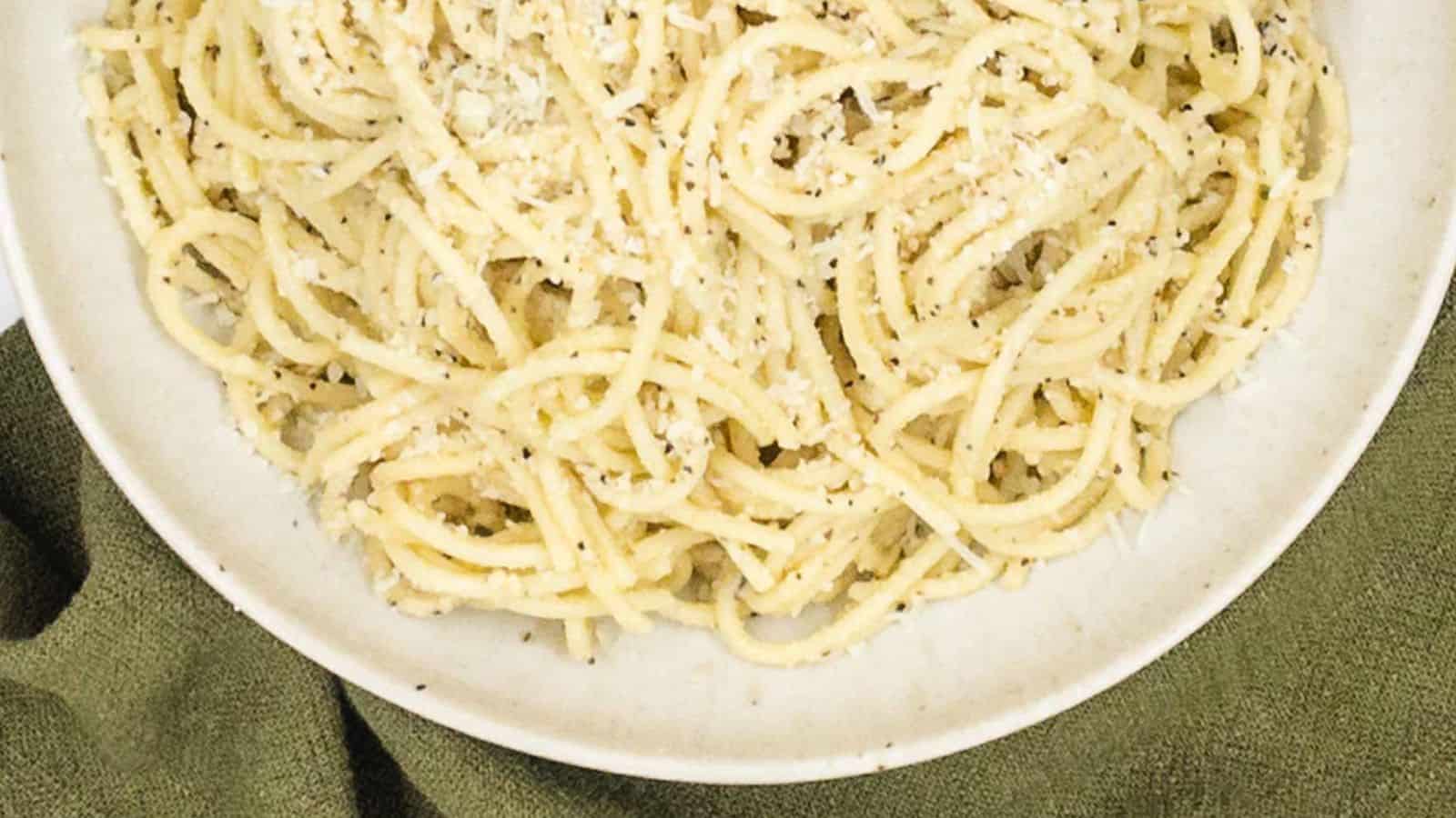 A plate of spaghetti with parmesan cheese on a green cloth.