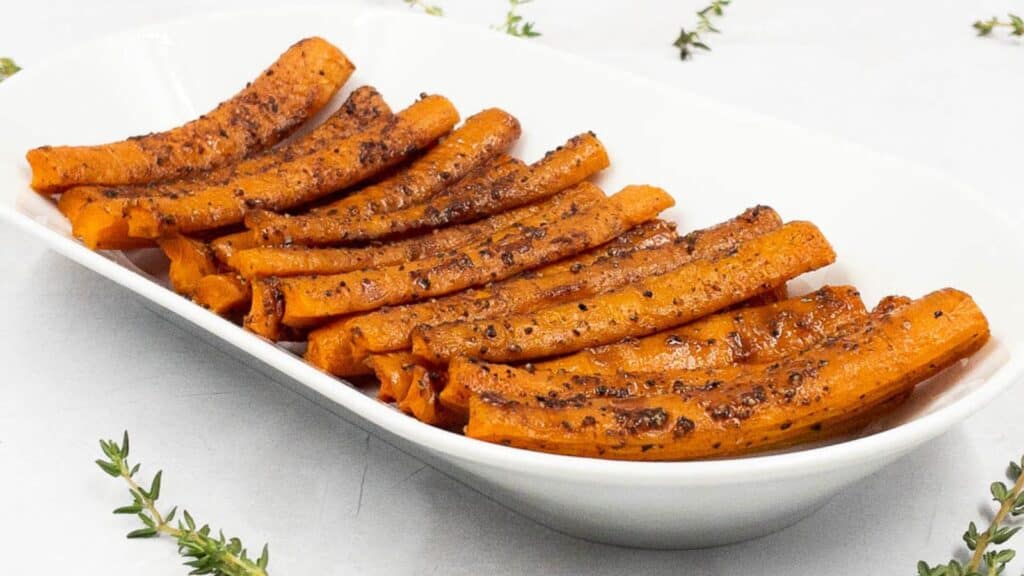 Roasted sweet potatoes in a white dish with sprigs of thyme.