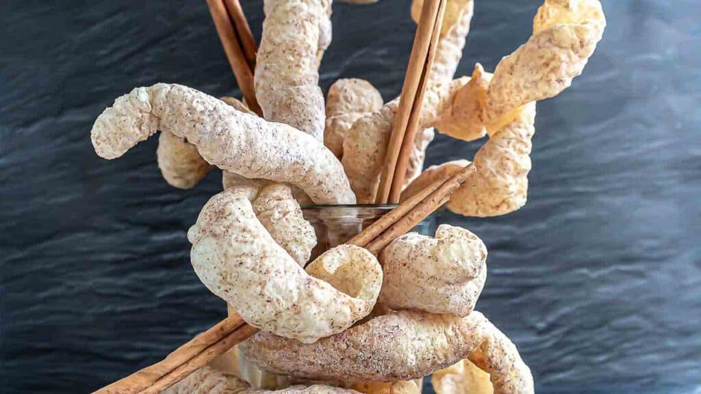 Keto Churro Pork Rinds - Chicharron inside glass with cinnamon sticks.