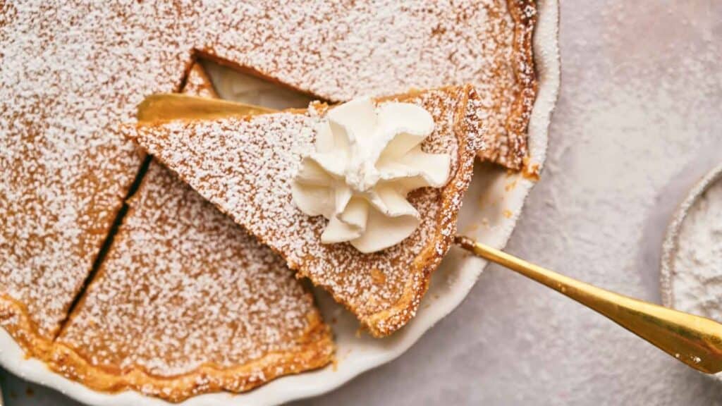 A slice of pumpkin pie with whipped cream and powdered sugar.