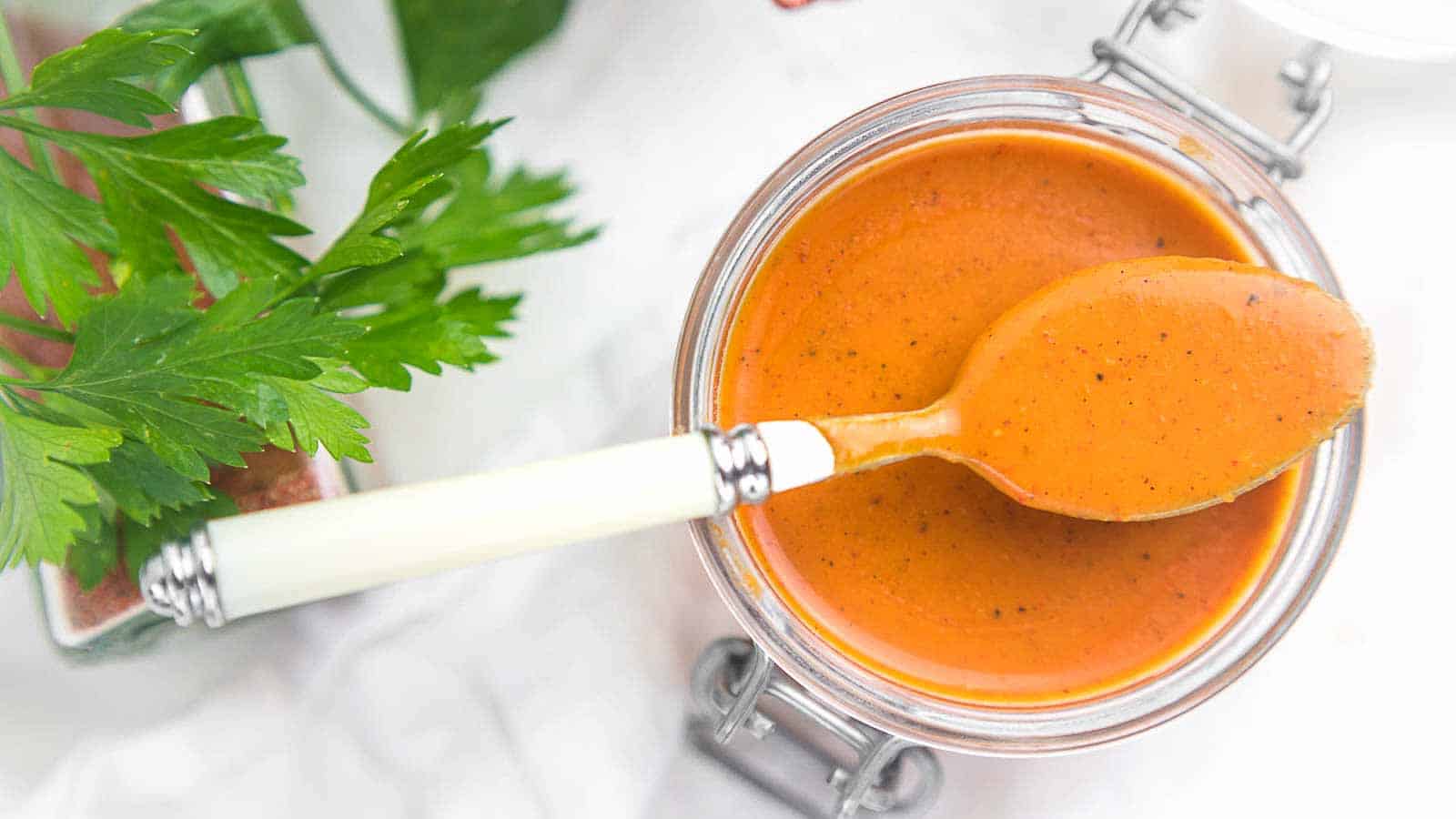 Enchilada Sauce in a glass container with a spoon on top. 