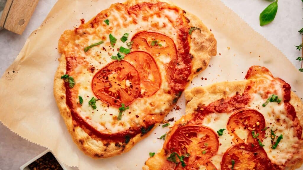 Two slices of pizza with tomatoes and herbs on a piece of paper.