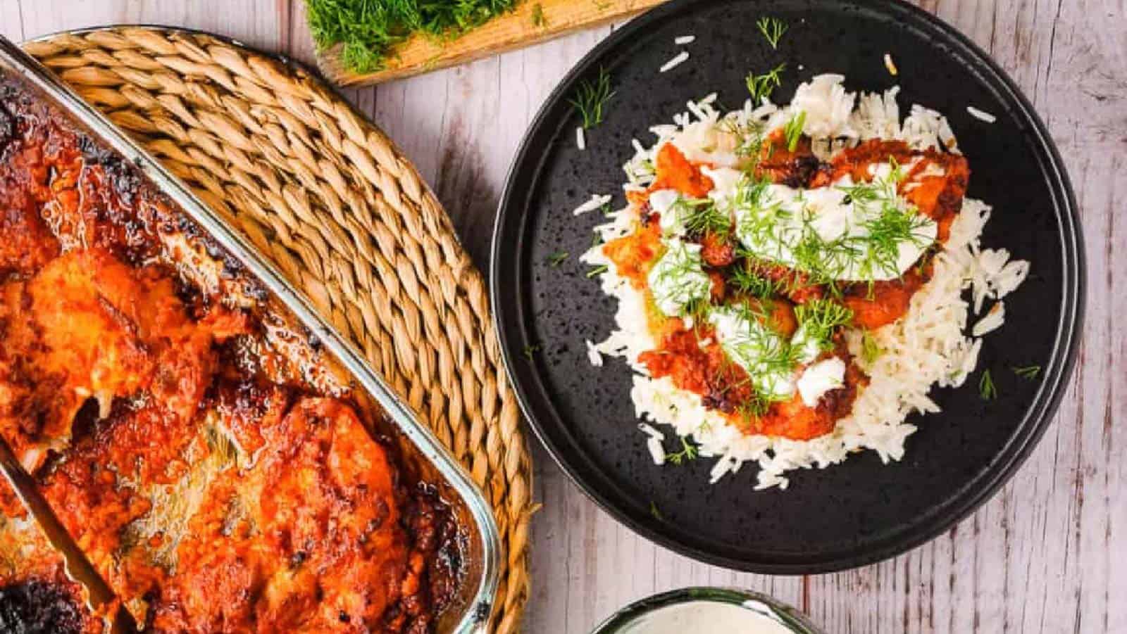 Harissa chicken in a baking pan with a plate of it over rice with yogurt and herbs on the side.