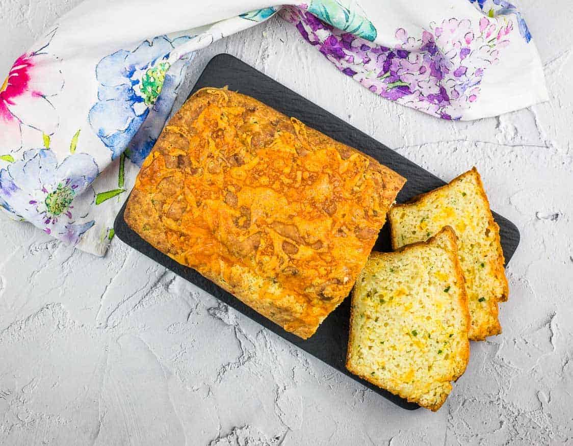 A top-down shot of Potato Cheese Bread with a few cut slices on a black platter.