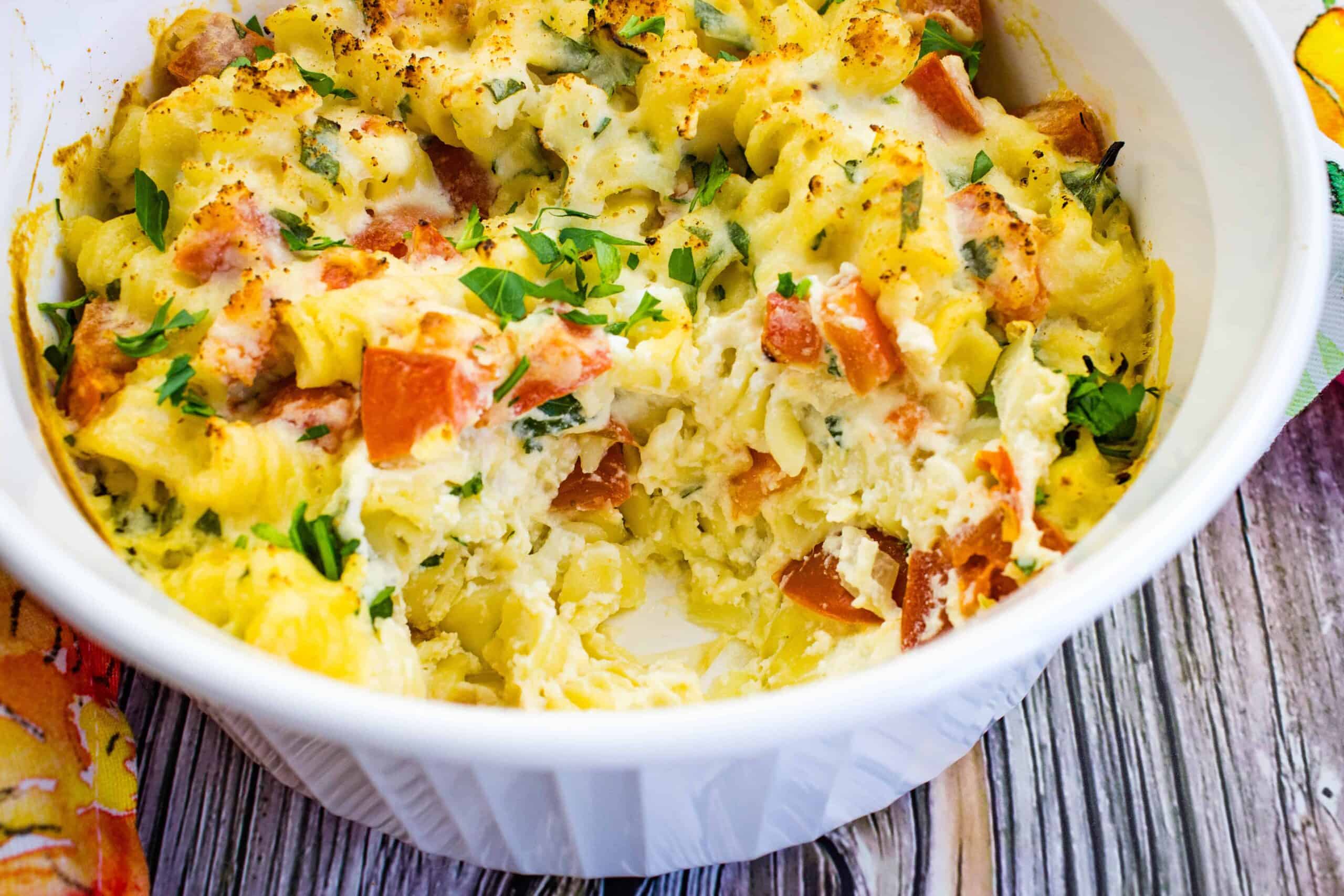 A closeup of a baking dish filled with Pasta with Ricotta and Tomatoes with a scoop missing.