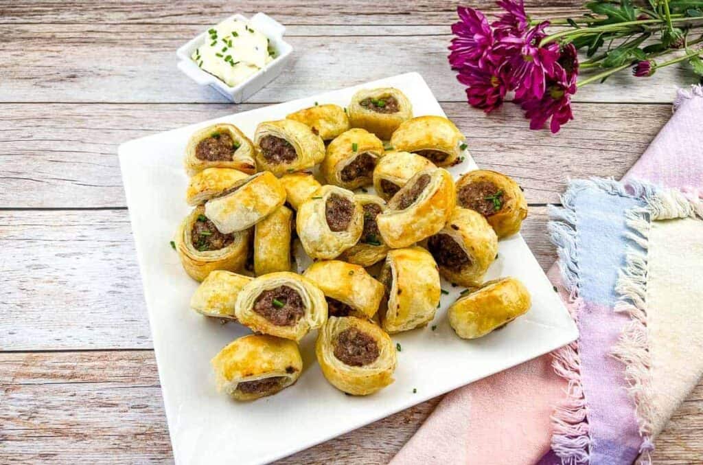 A plate of Sausage Rolls with dip in the background.