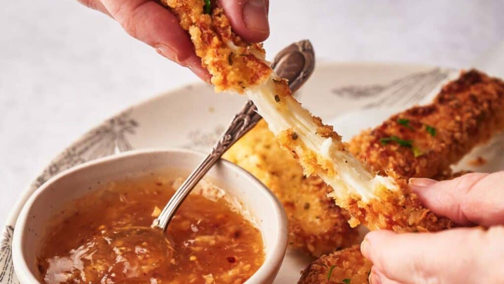 A person is dipping chicken sticks into a sauce.