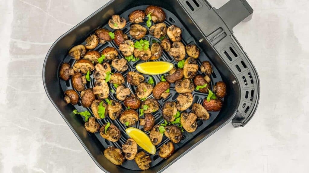 A frying pan filled with mushrooms and lemon wedges.