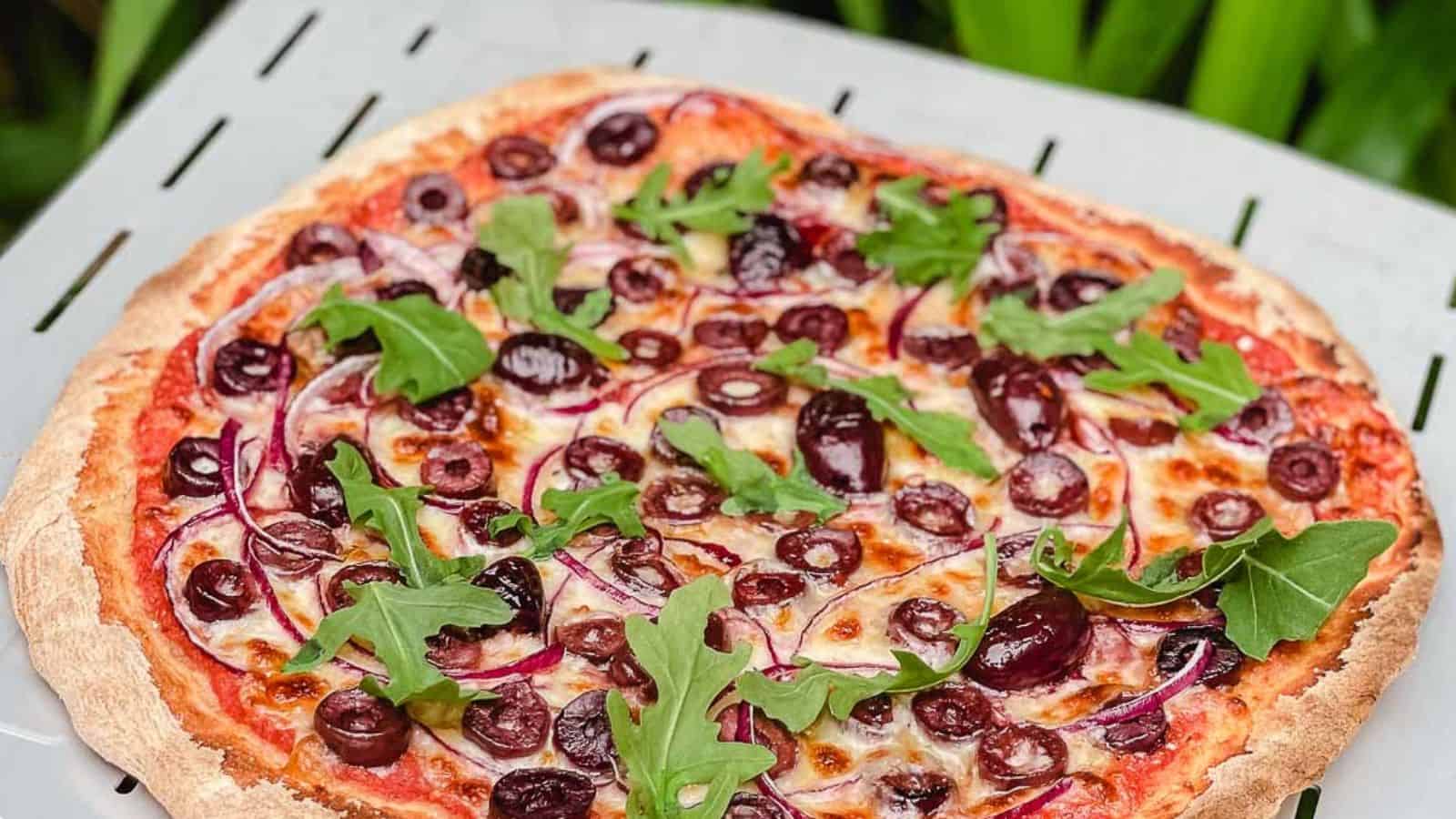 Cooked olive pizza on a pizza paddle.