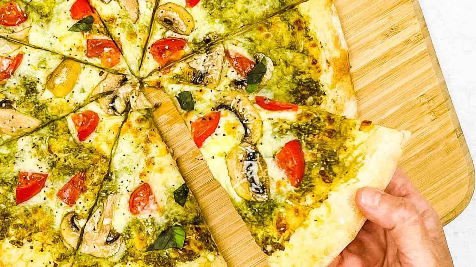 Someone grabbing a slice of pesto pizza.