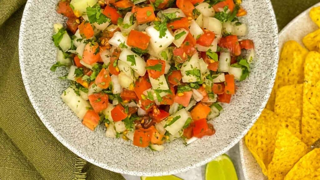 A bowl of mexican vegetable salsa with tortilla chips.