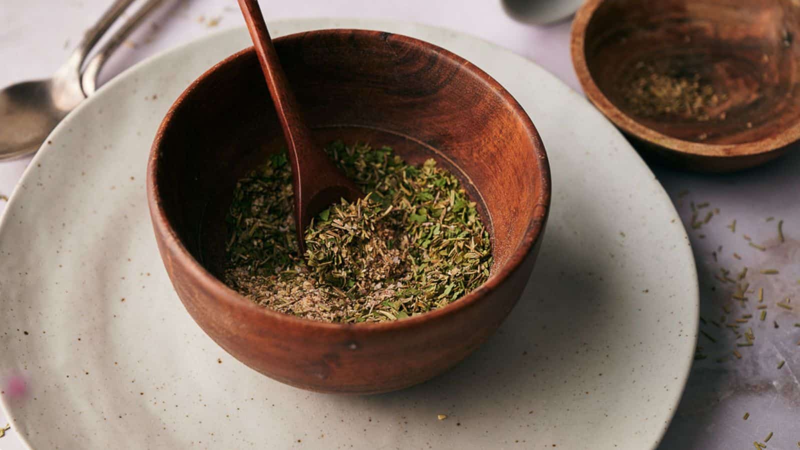 A wooden bowl filled with pizza seasoning on a plate.