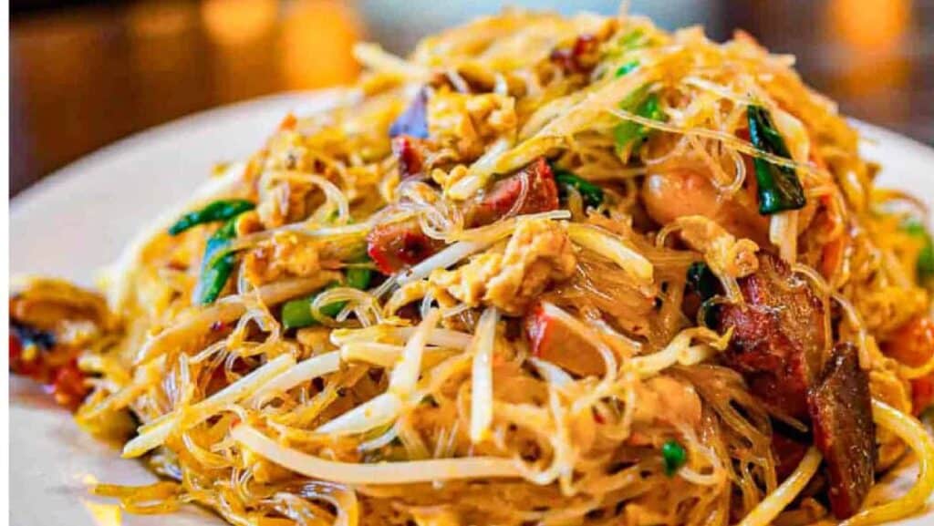 Rice noodles with meat and veggies on a white plate.