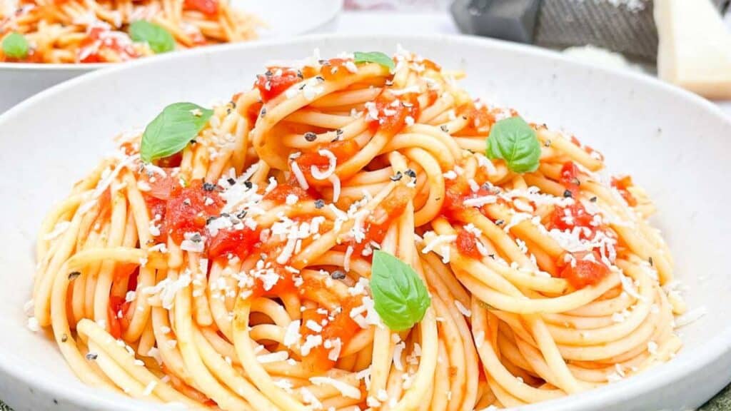 Spaghetti with tomatoes and basil in a white bowl.