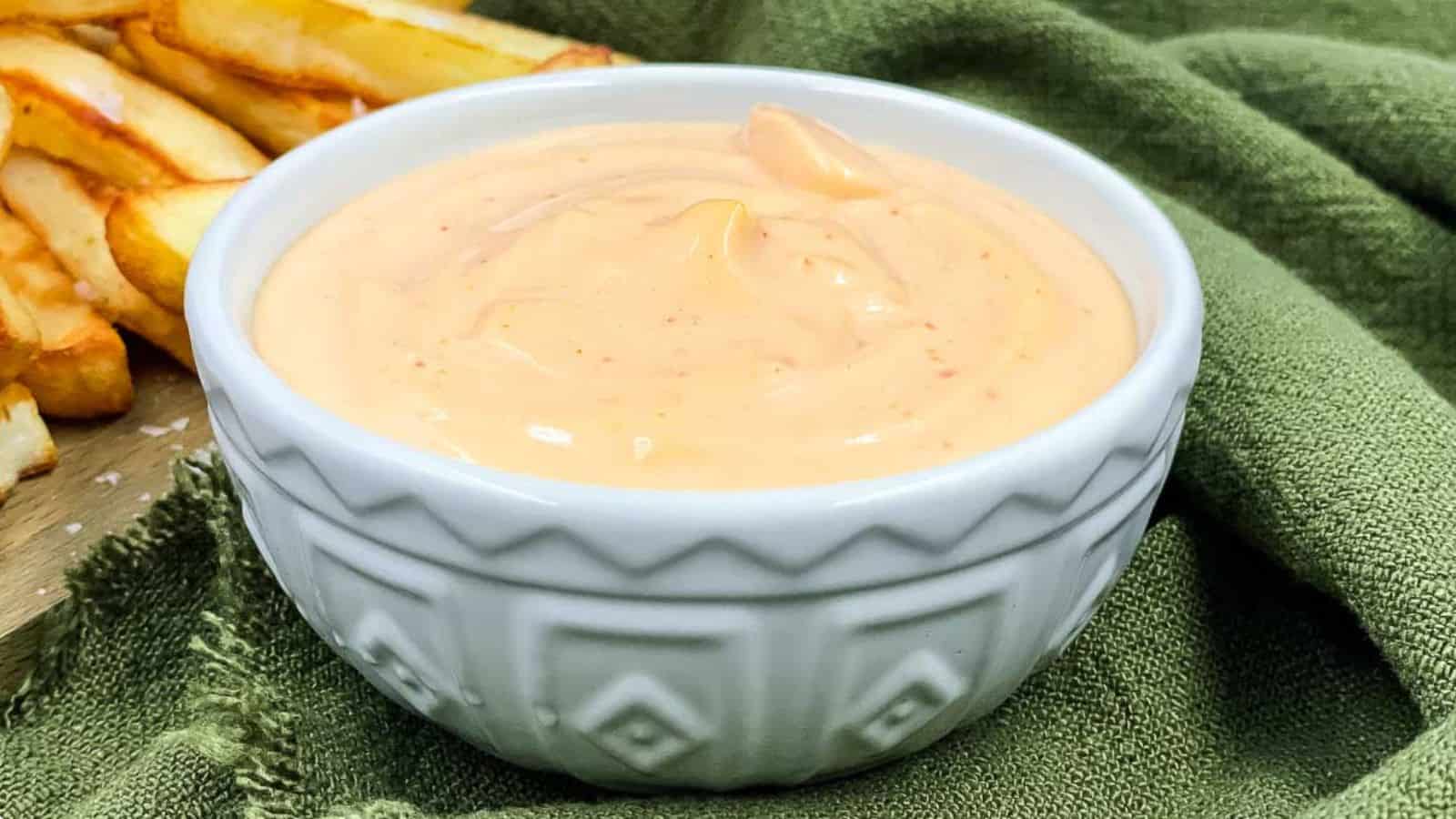 Sriracha aioli in a serving bowl and fries by the side of it.