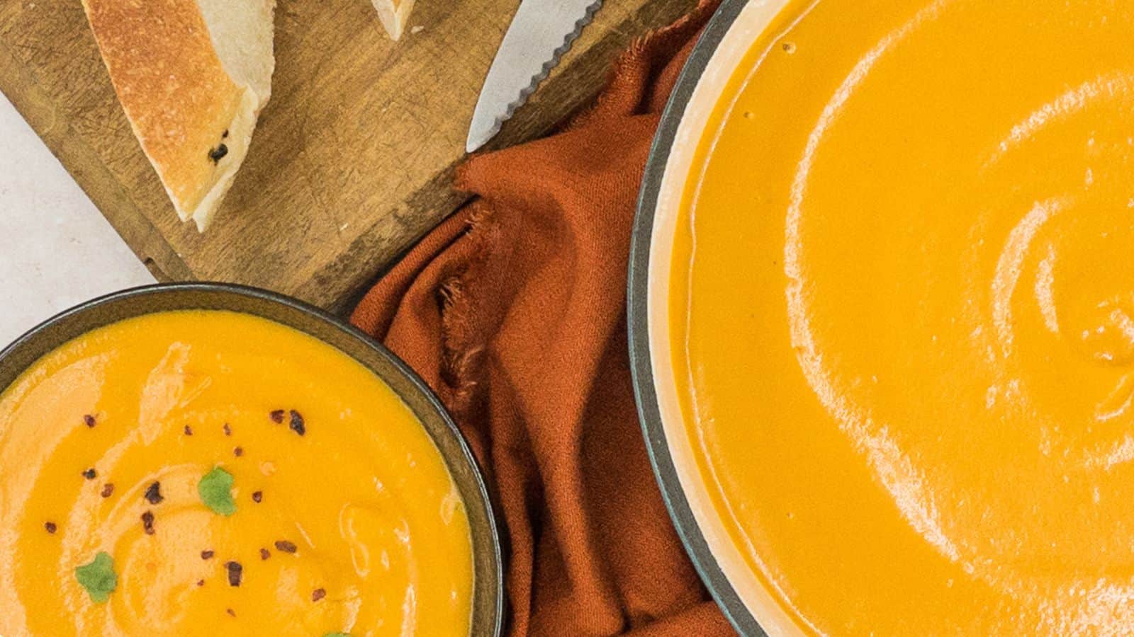 A bowl of sweet potato soup with bread next to it.