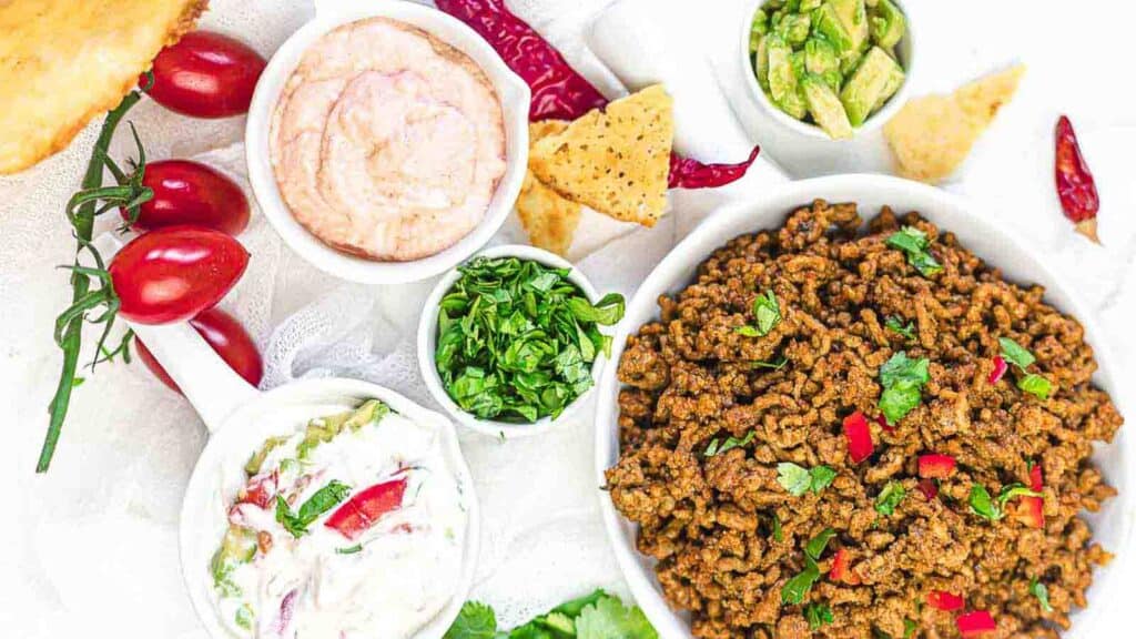 Ground Beef Taco Meat inside a white plate with smaller bowls of veggies and sauces.