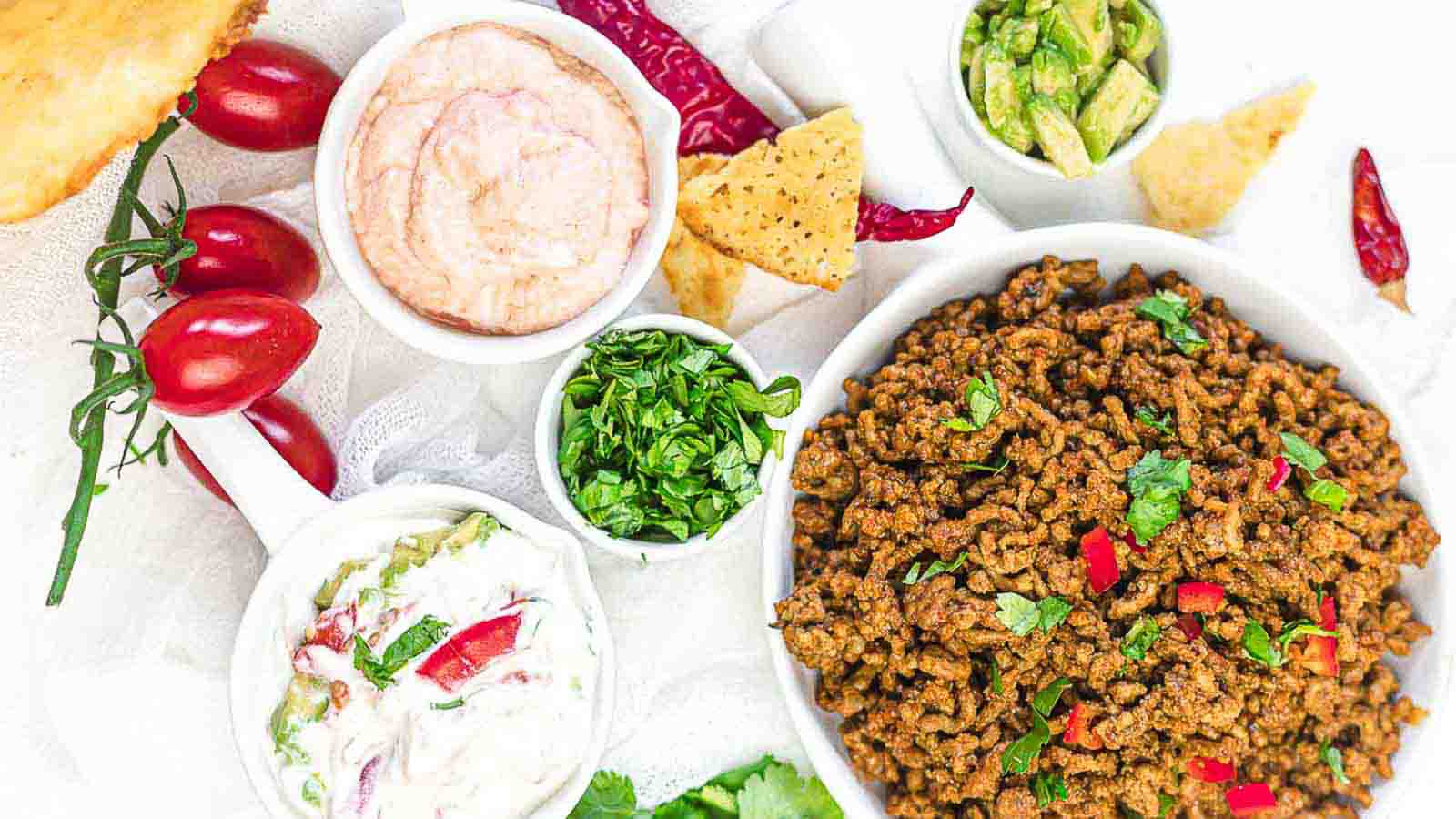 Ground Beef Taco Meat inside a white plate with smaller bowls of veggies and sauces. 