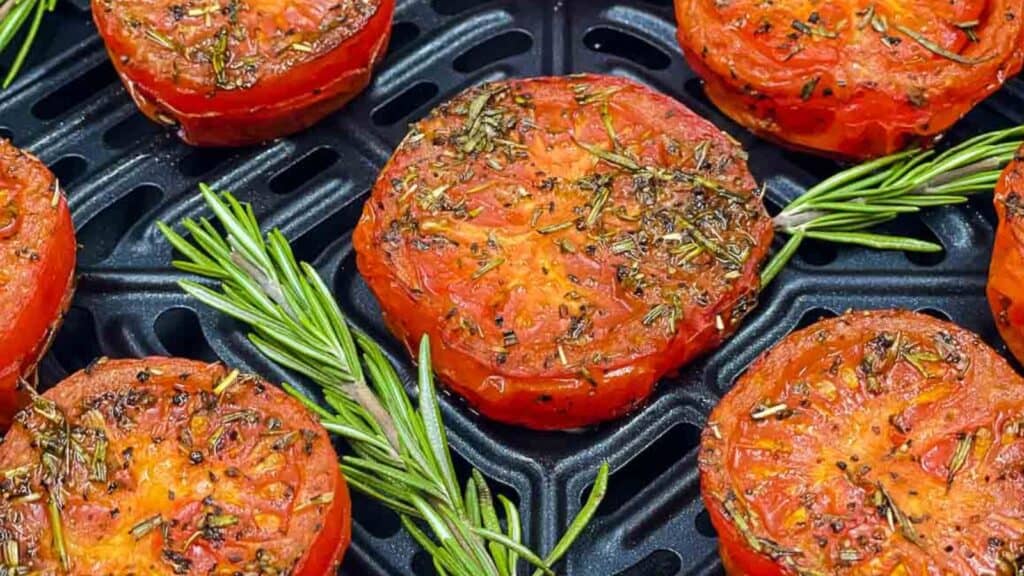 Roasted tomatoes on a grill with rosemary sprigs.