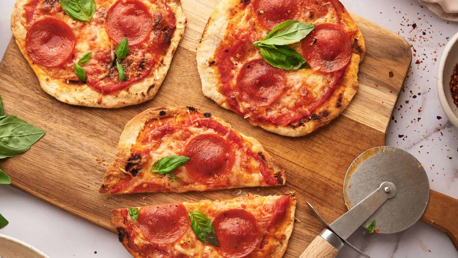 Four tortilla pizzas on a wooden cutting board.