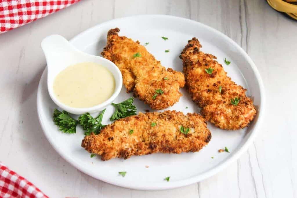 Fried chicken tenders on a white plate with dipping sauce.