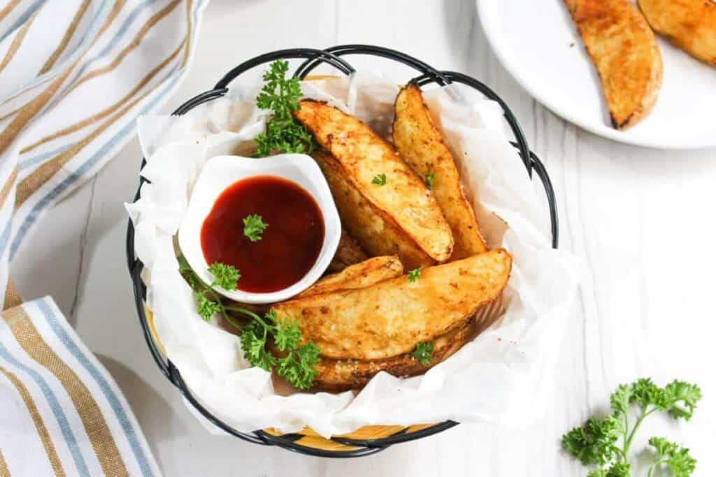 Fried potato wedges in a basket with ketchup.