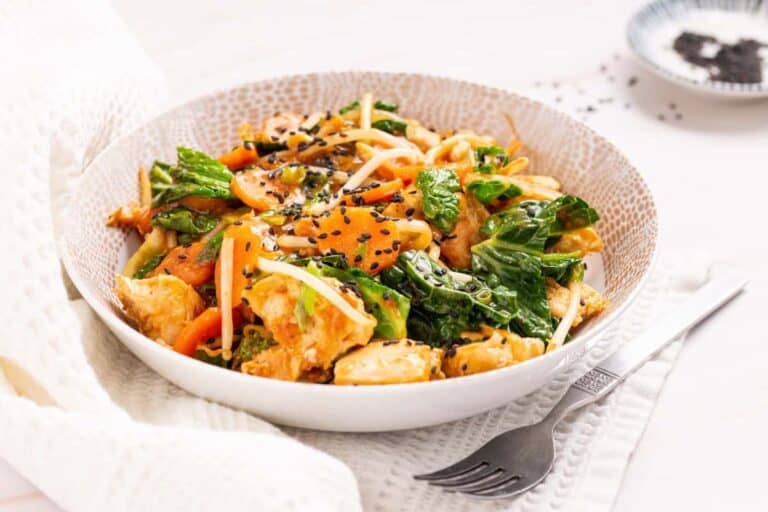 A bowl of chicken and kale in a white bowl with a fork.