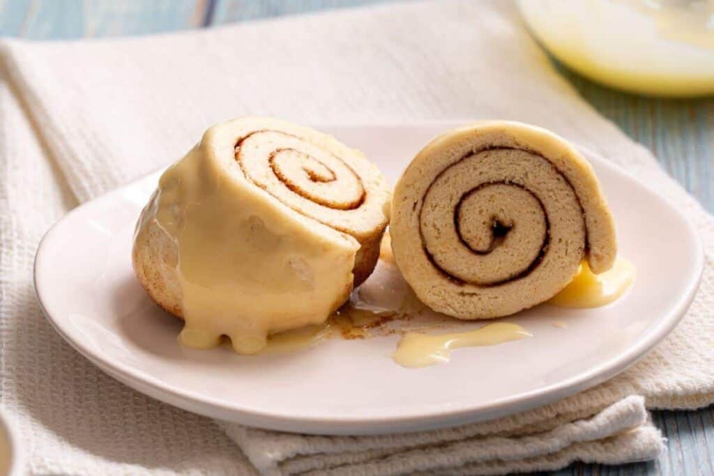 Cinnamon roll made in a mug sliced in half on plate.