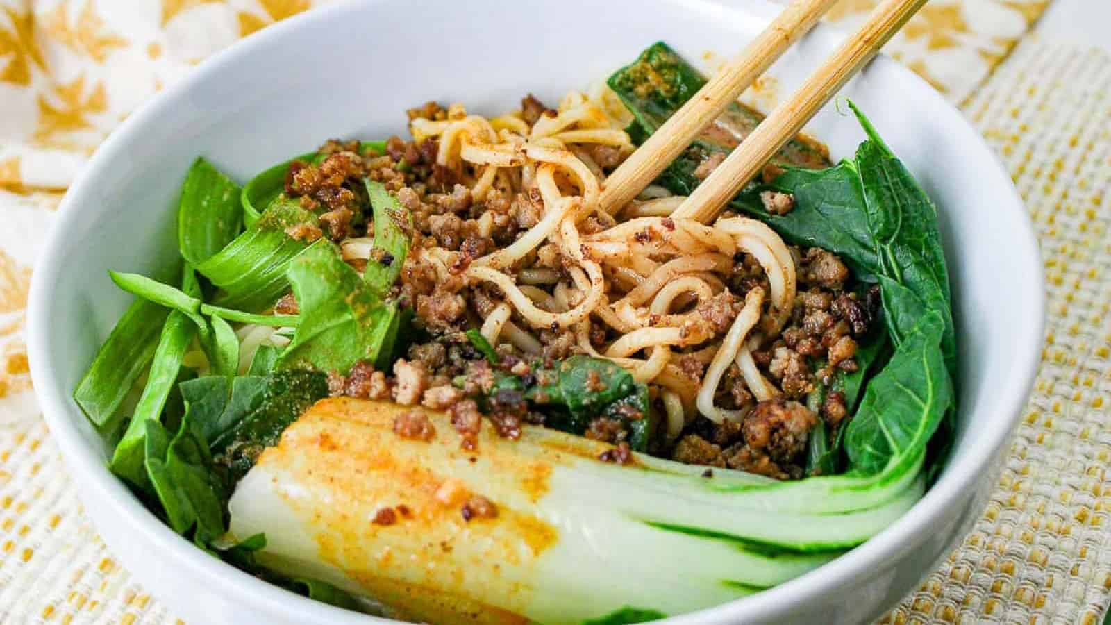 Dan dan noodles in a white bowl with chopsticks.