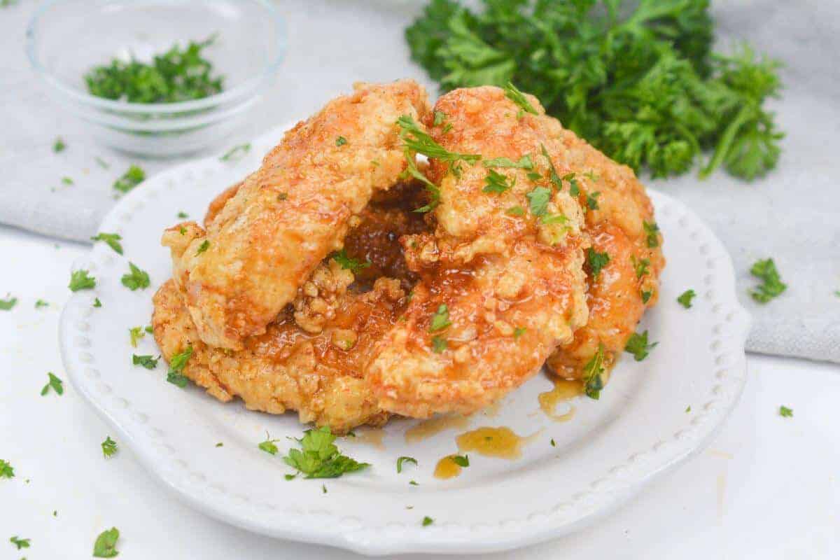 Serving of honey butter chicken garnished with parsley on plate.