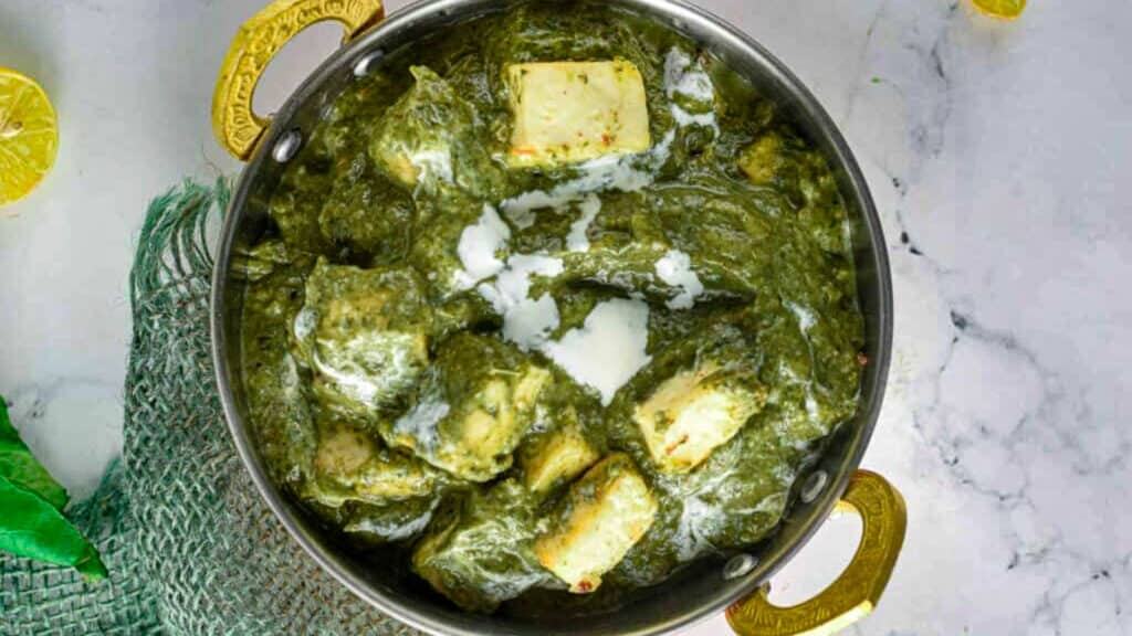 A bowl of green curry with tofu and lemons.