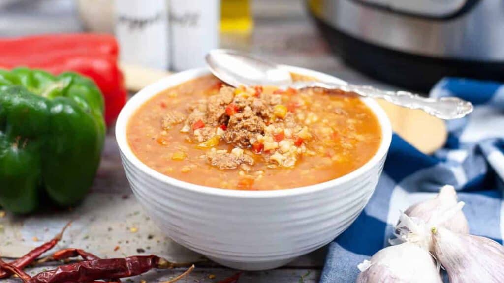 A bowl of soup with peppers and garlic in front of an instant pot.