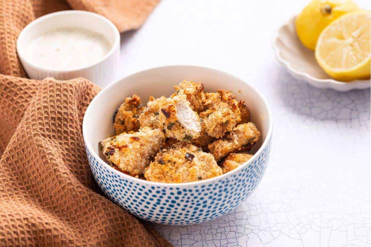 Popcorn chicken in bowl with one piece cut to show inside.