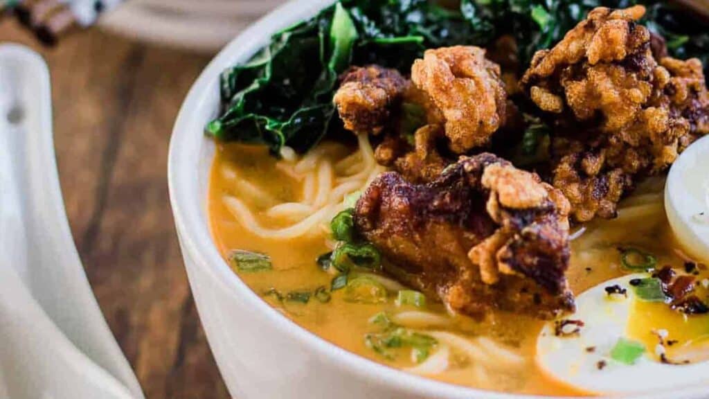 A bowl of chicken noodle soup with eggs and greens.