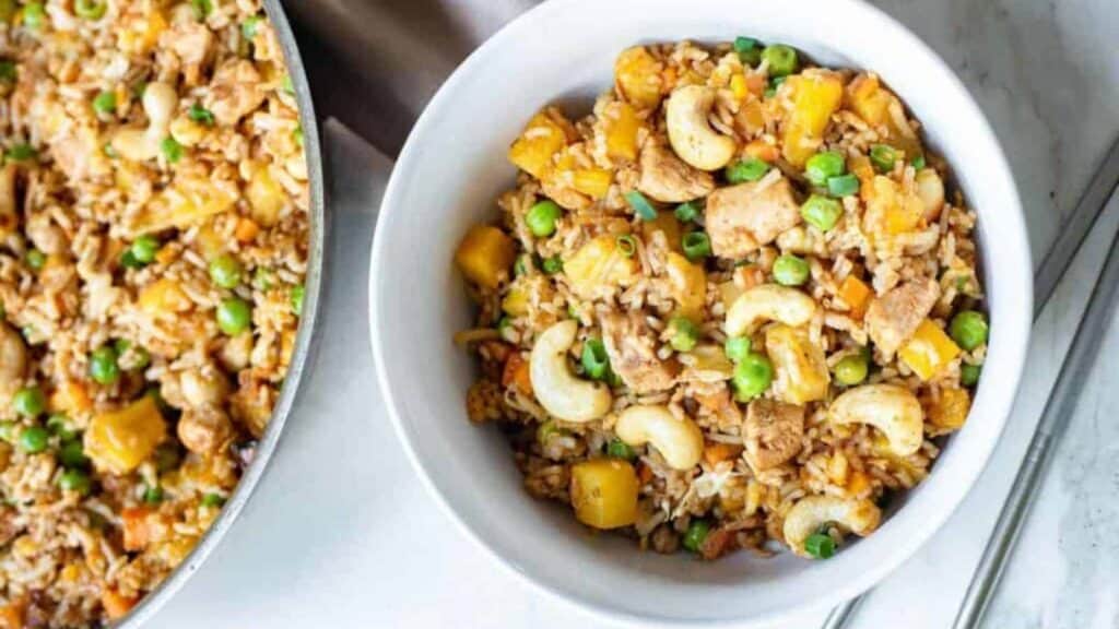 Overhead shot of Thai fried rice in a white bowl with a skillet of fried rice on the side.