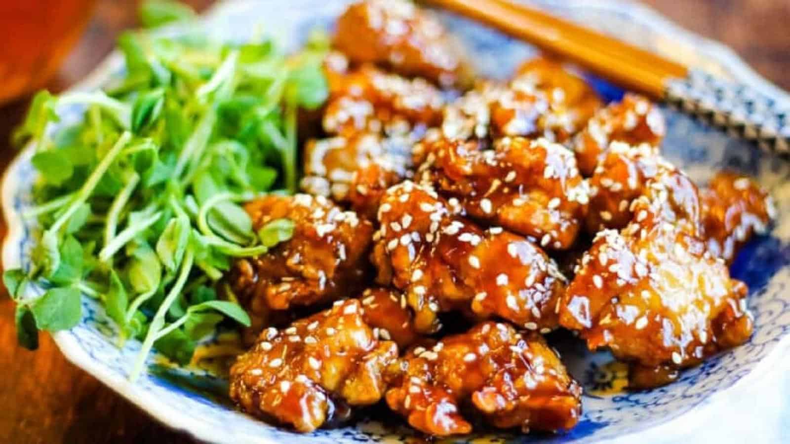 low angle shot of a plate of fried chicken with sesame sauce and sesame seeds.