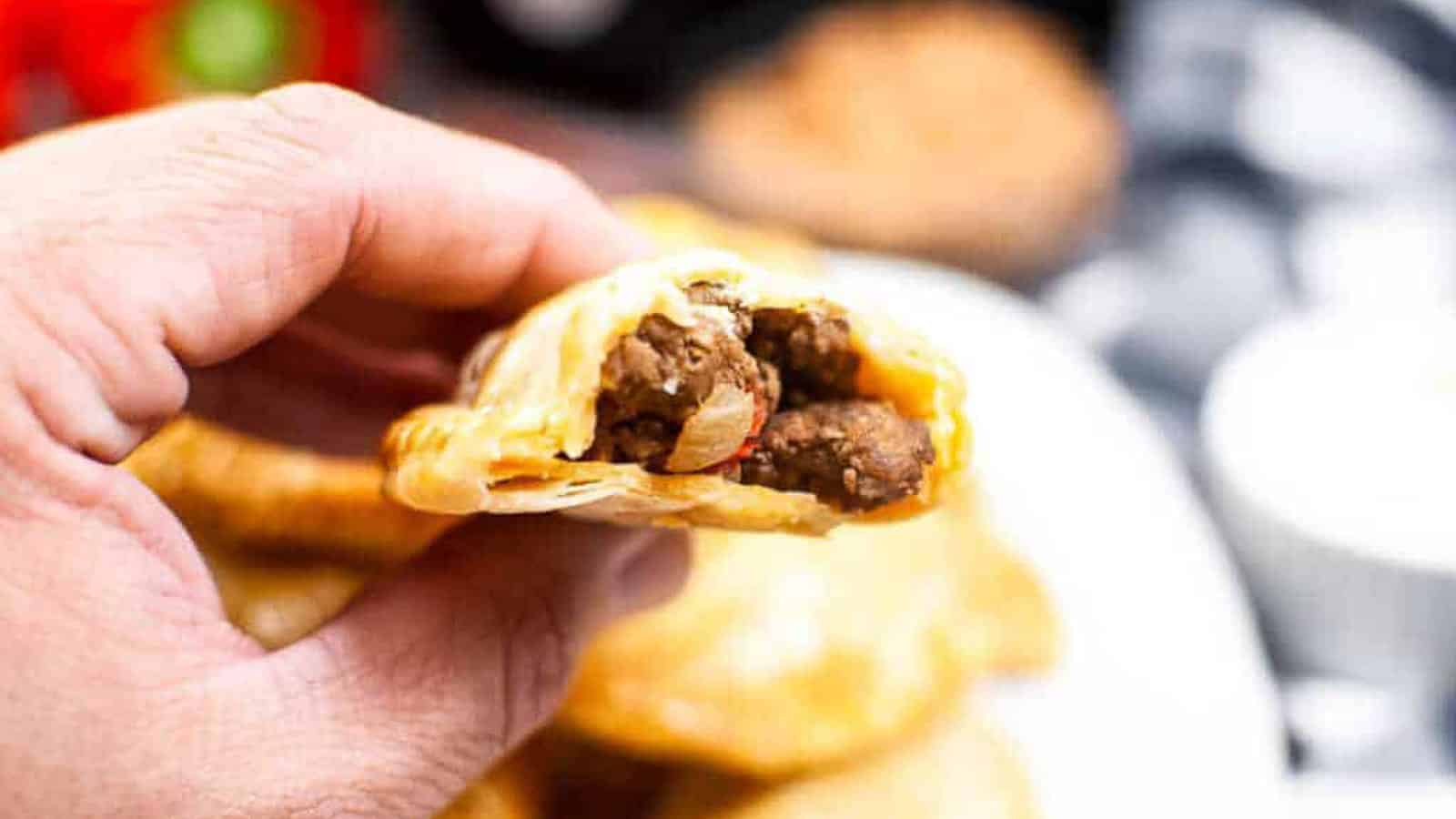 A hand holding a n empanada that is broken open so you can see the inside filling.