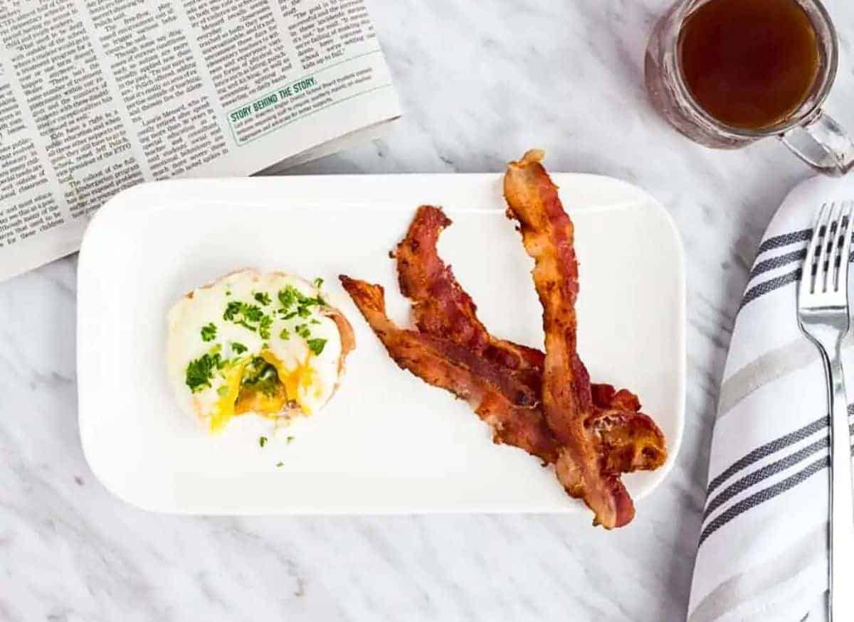 Bacon and eggs on a plate with a cup of coffee.