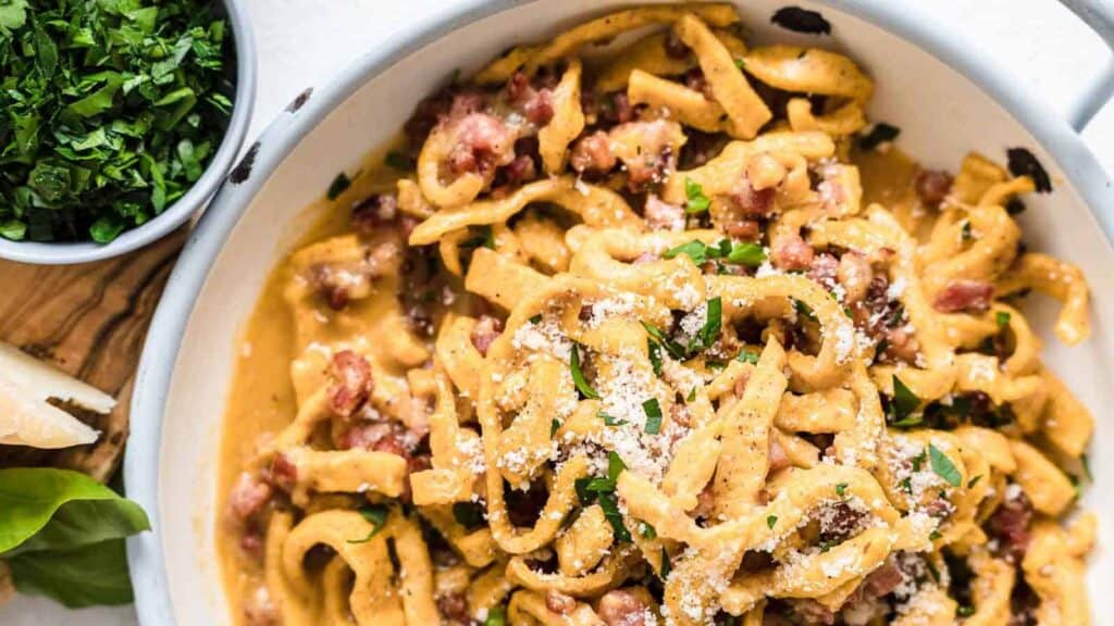 Pasta Carbonara inside a bowl with herbs and bacon.