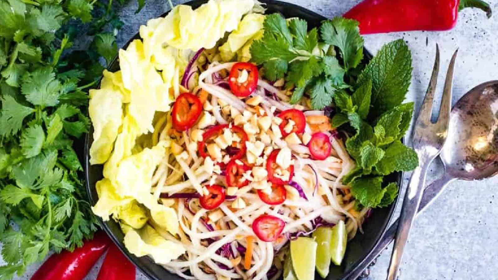 Overhead shot of green papaya salad in a black bowl.