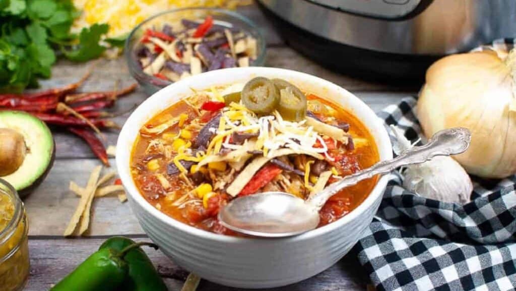 Low angle shot of a white bowl filled with tortilla soup. There is an instant pot in the background.